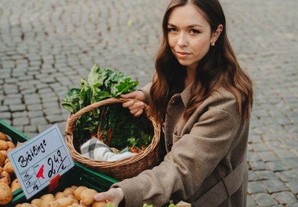 Young woman shopping at Erfurt farmers market, holding basket with fresh vegetables. Capturing local shopping culture.