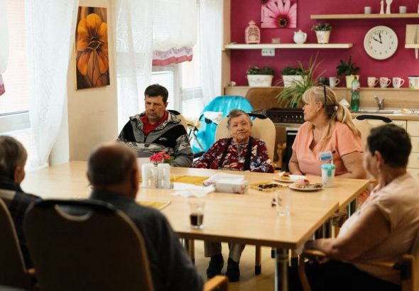 Seniors enjoying a meal in a nursing home dining room with caregivers in Karviná, Czechia.