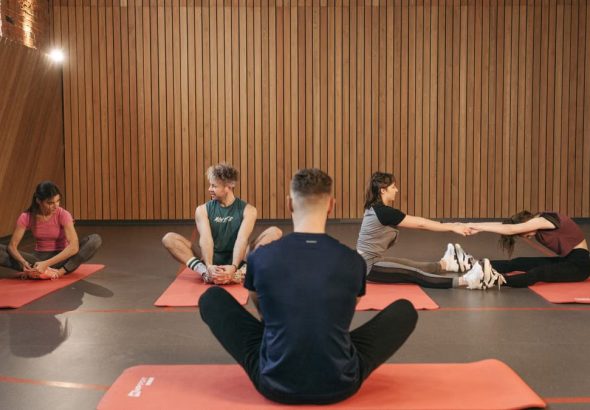 A group of adults practicing yoga and stretching on mats in a wooden panelled room.